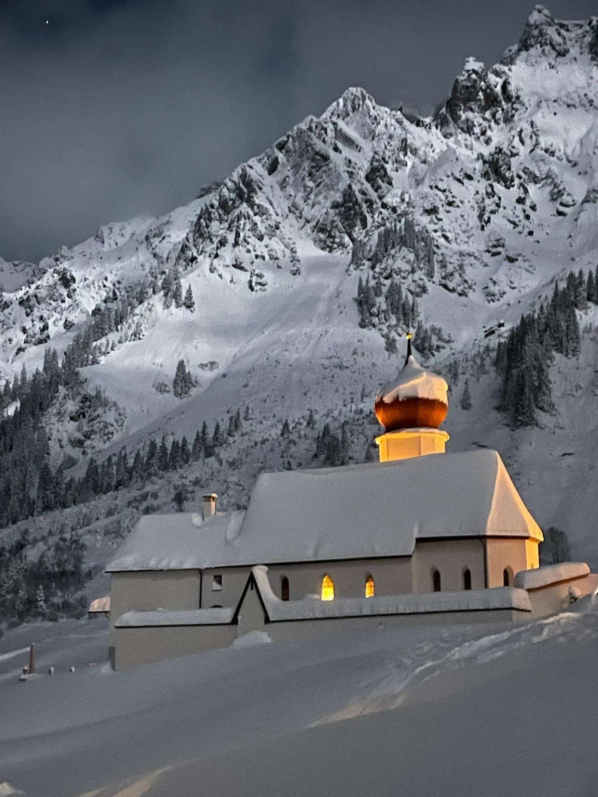 Snowy surroundings of the motel with a chapel and mountains