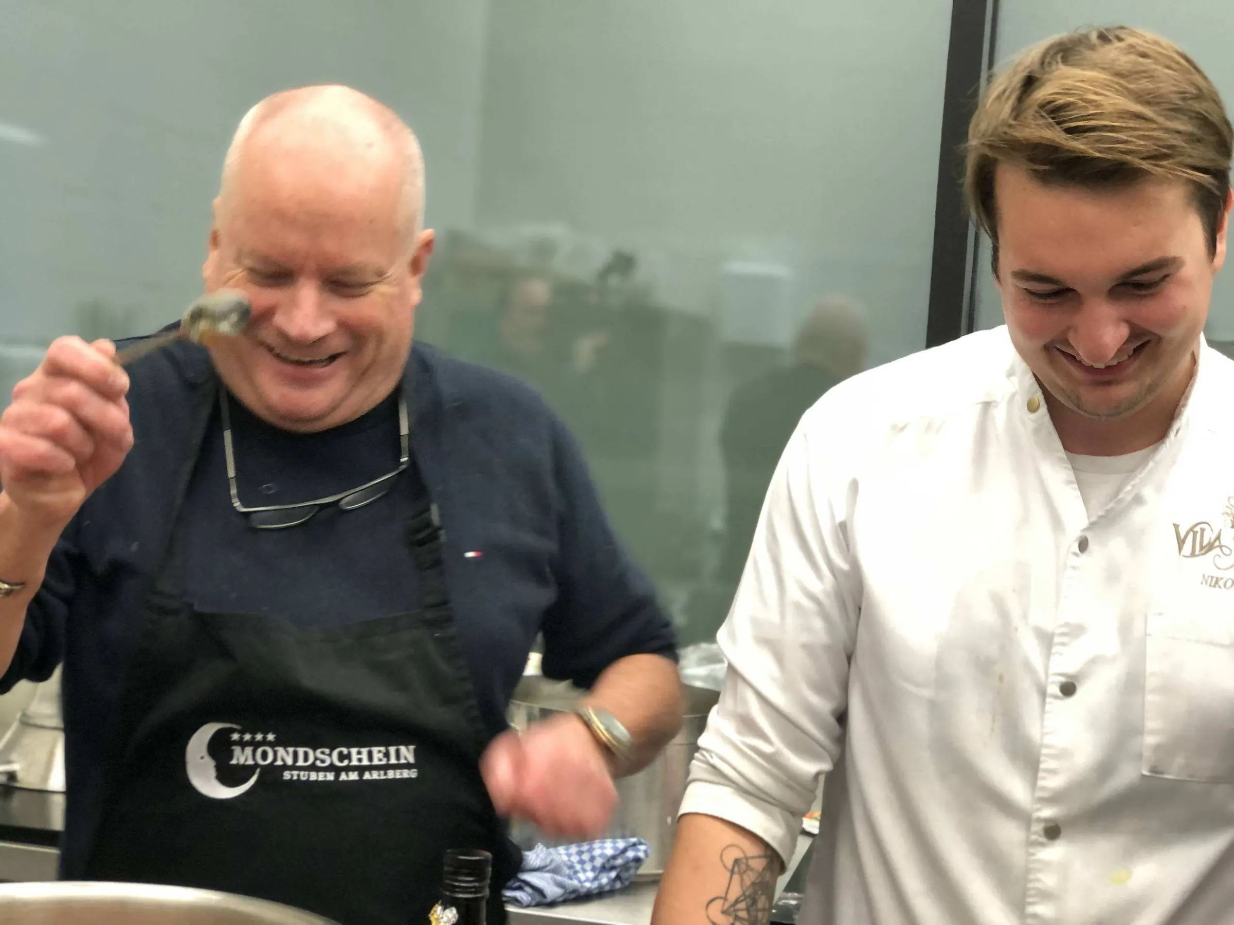 Een kok proeft lachend samen met een jonge collega