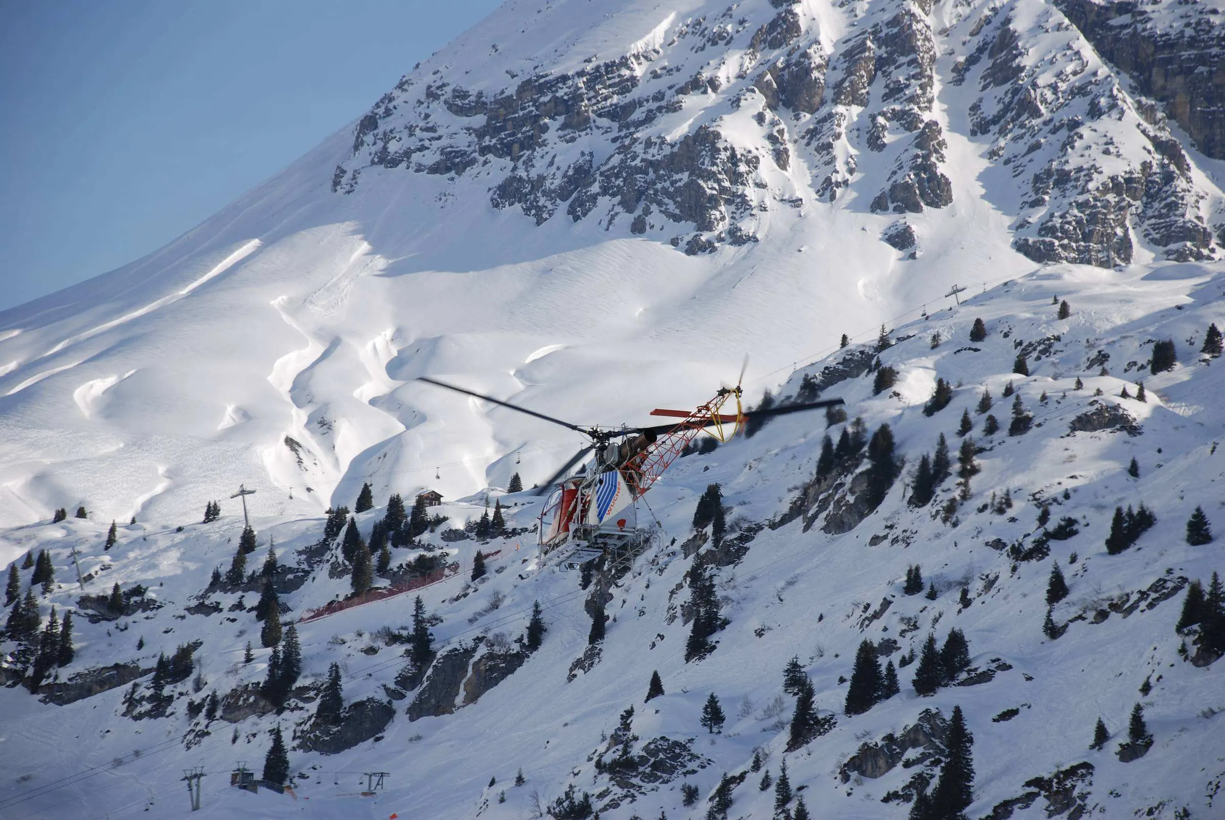Helikopter vliegt langs een besneeuwde bergflank
