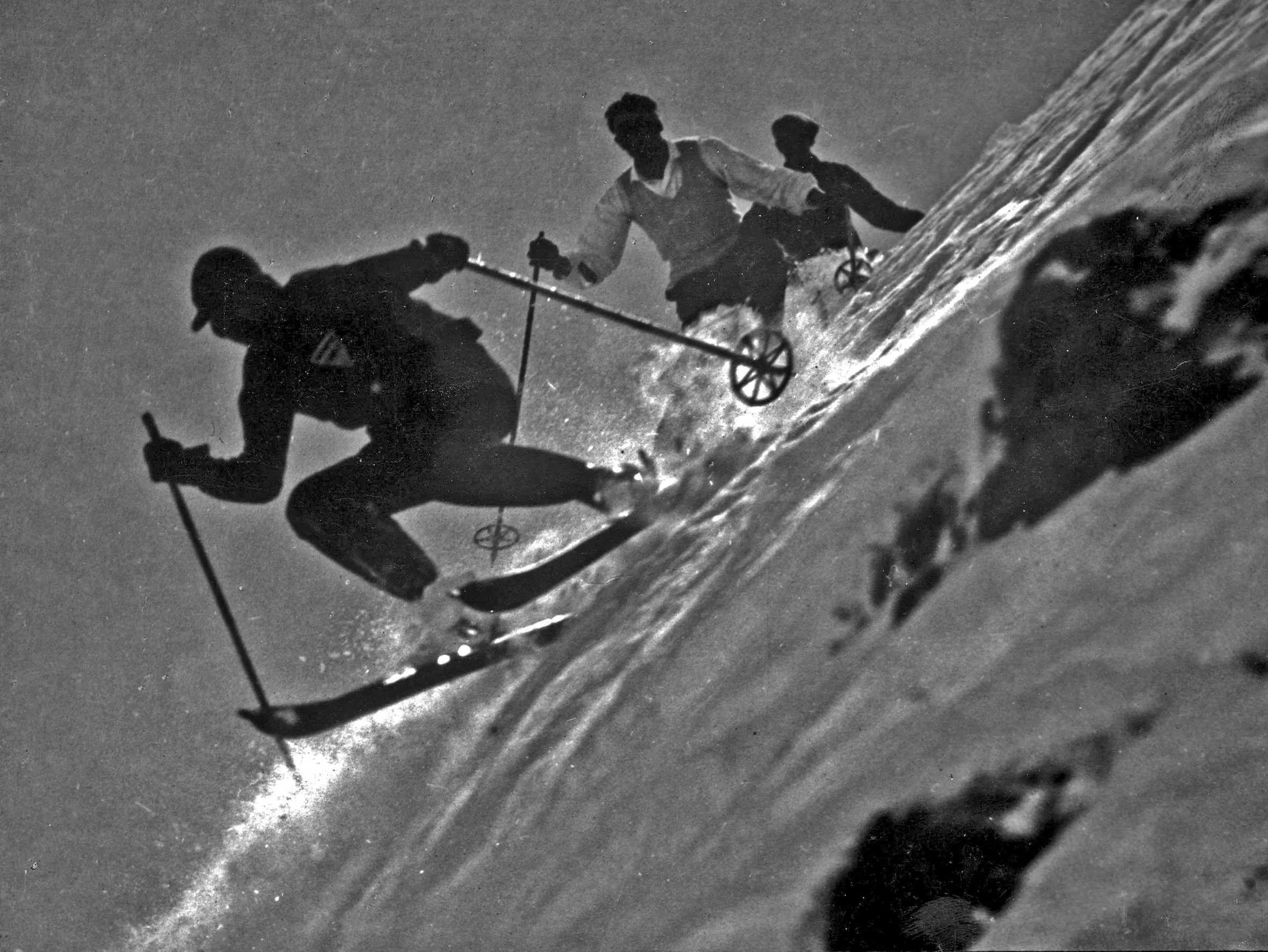 Skiers deep in a turn on a steep slope, historic photo