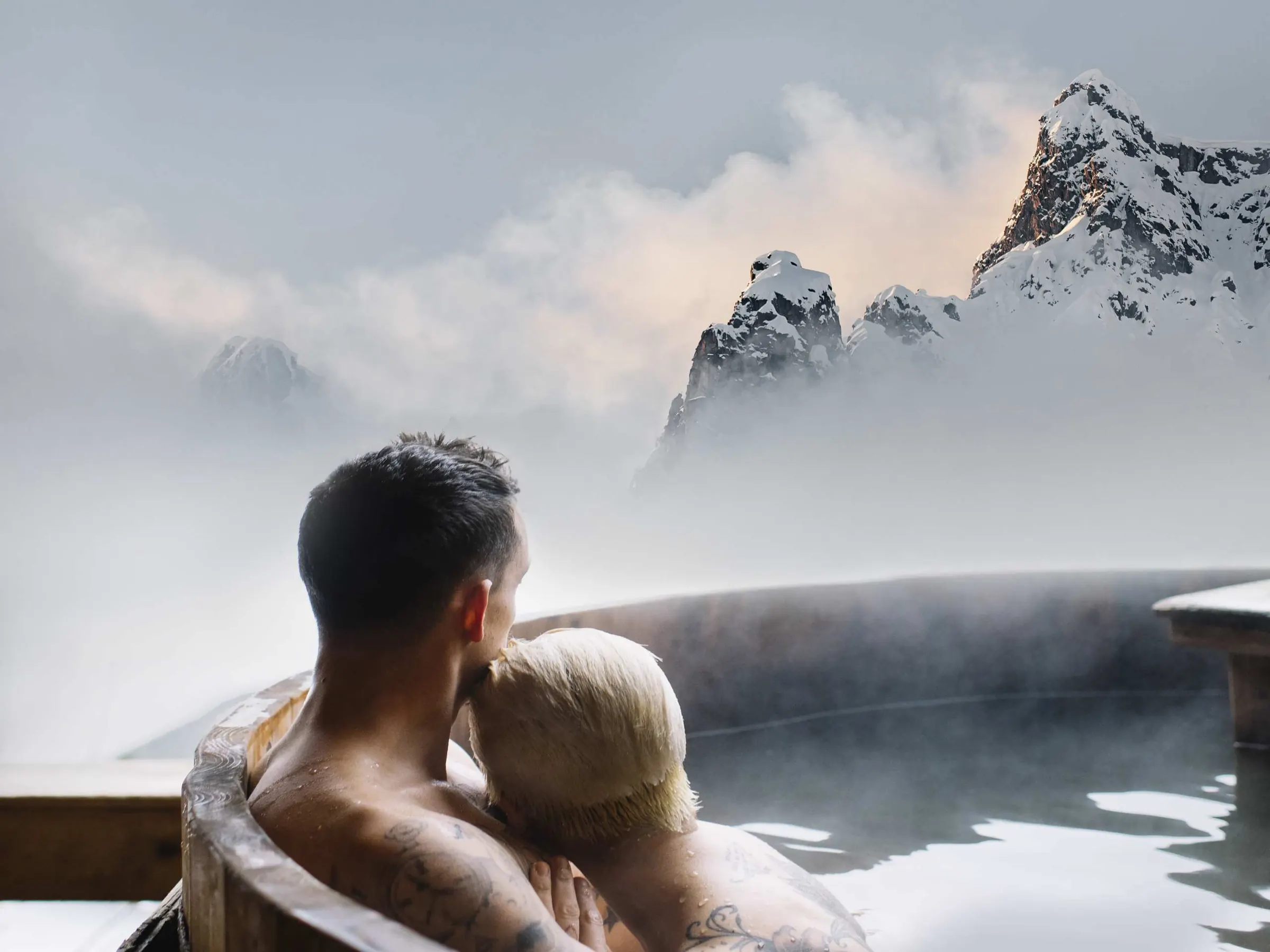 Couple in the hot tub of the chalet suite, mountains in the mist behind