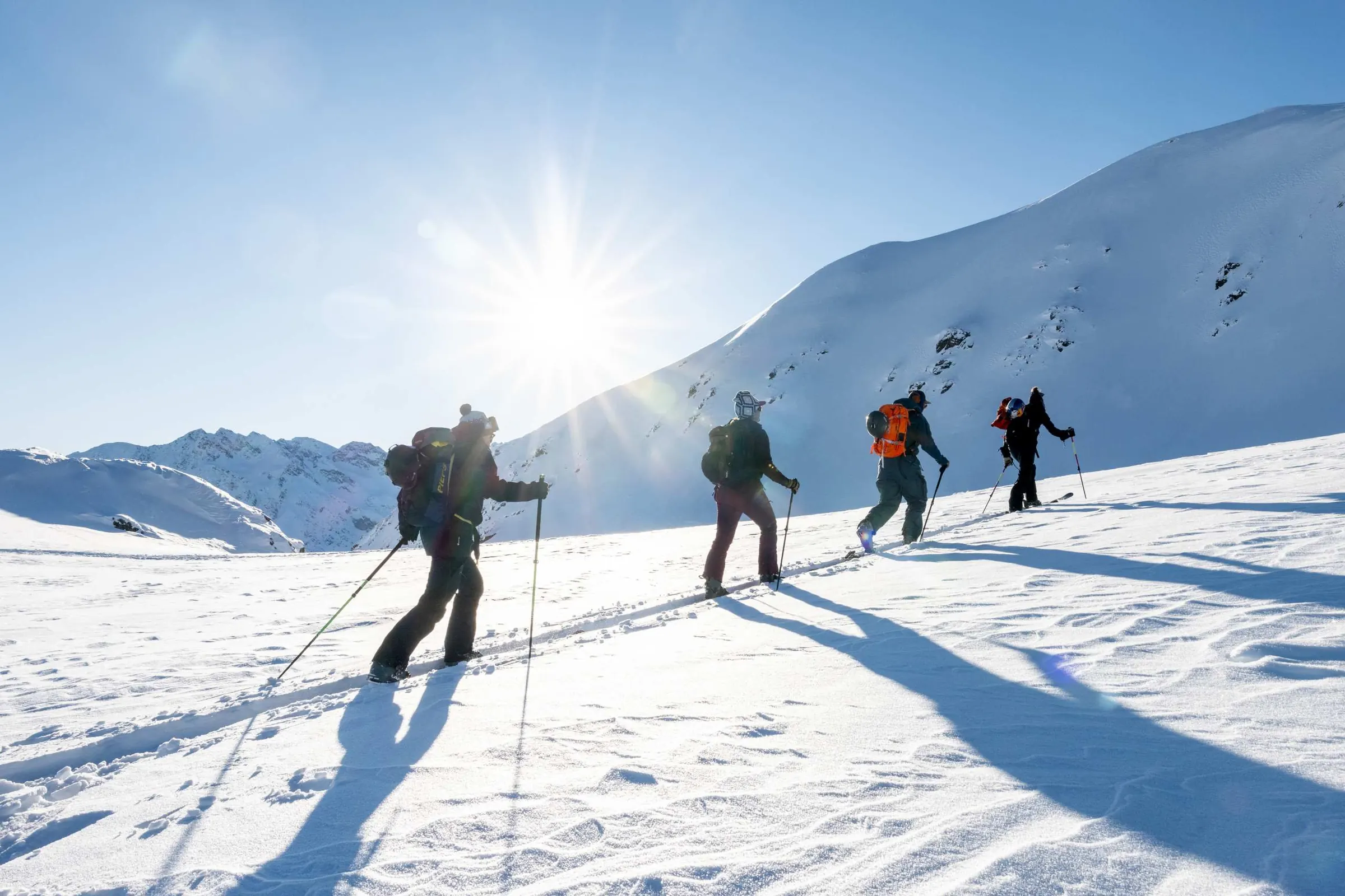 Toerskiërs klimmen achter elkaar tegen de zon in
