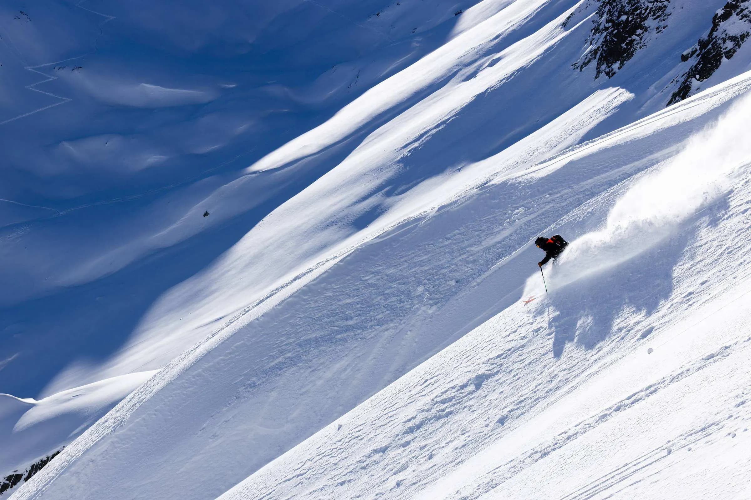 Skiër in een steile poederhelling met lange schaduwen