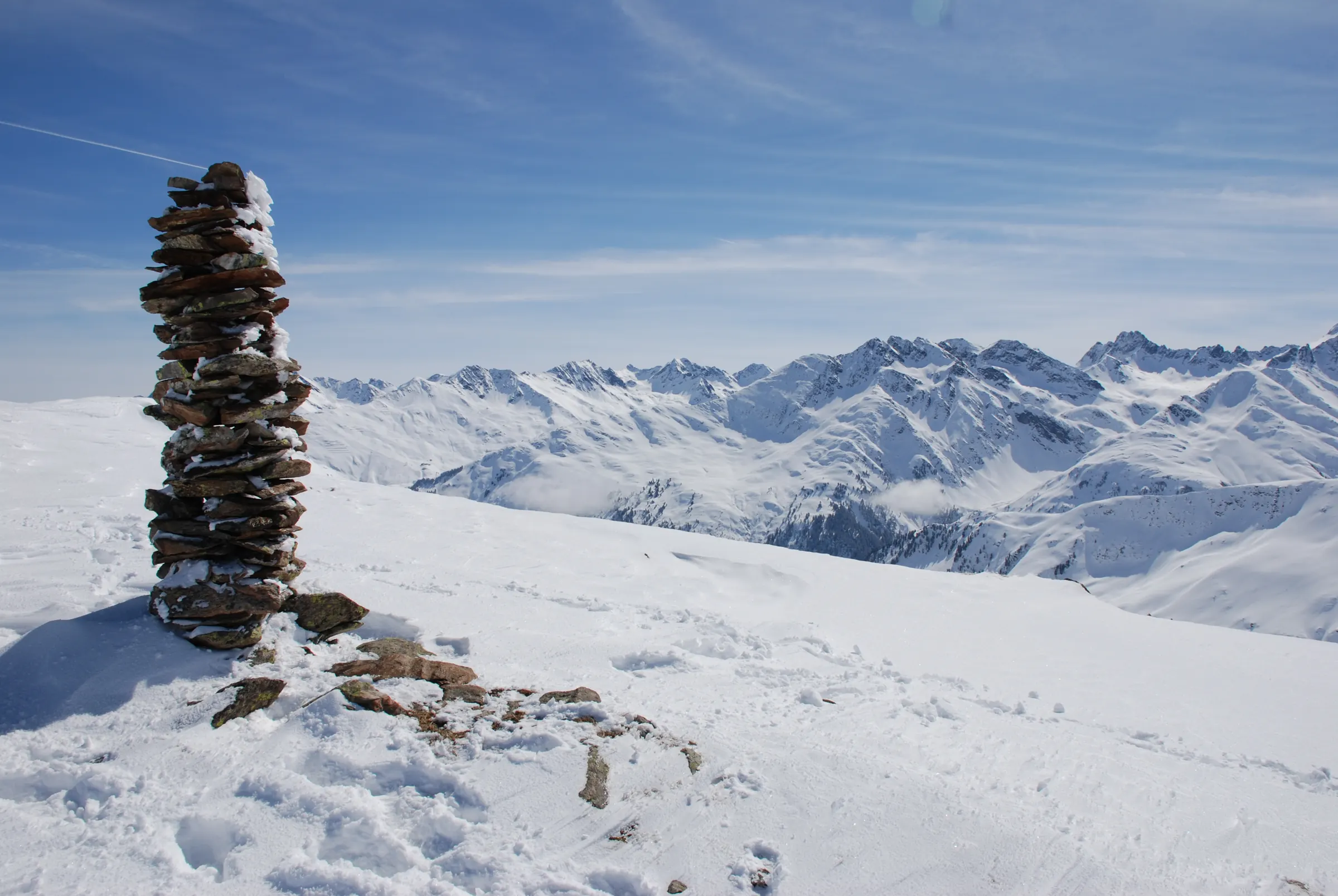 Steenmannetje op een top met zicht over de besneeuwde Alpen