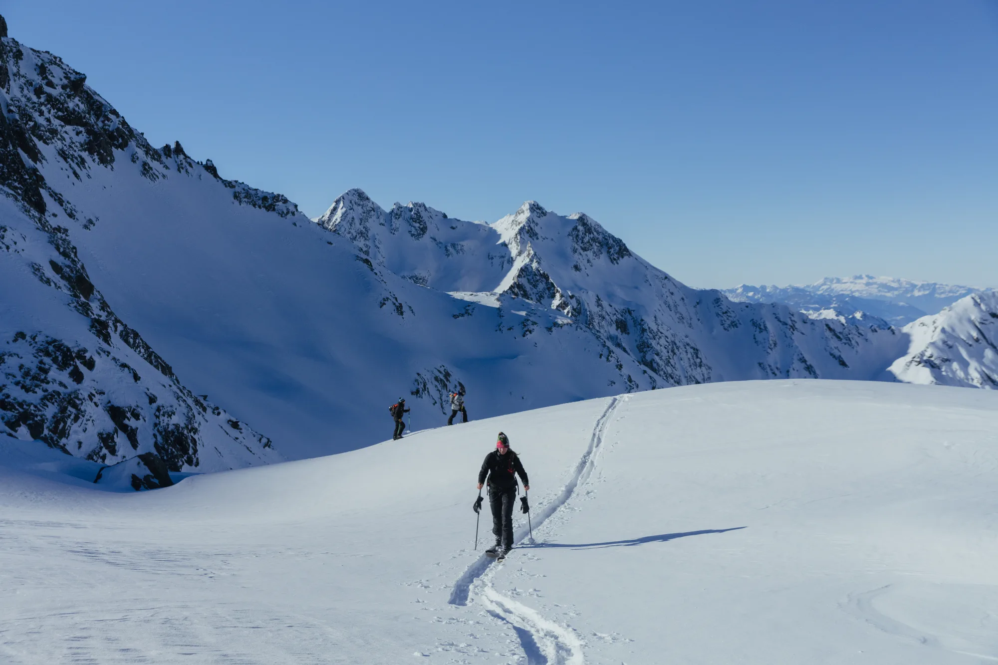 Ski mountaineers trekking through untouched snow fields beneath rugged alpine peaks under a clear blue sky – photo by Alexander Fuchs
