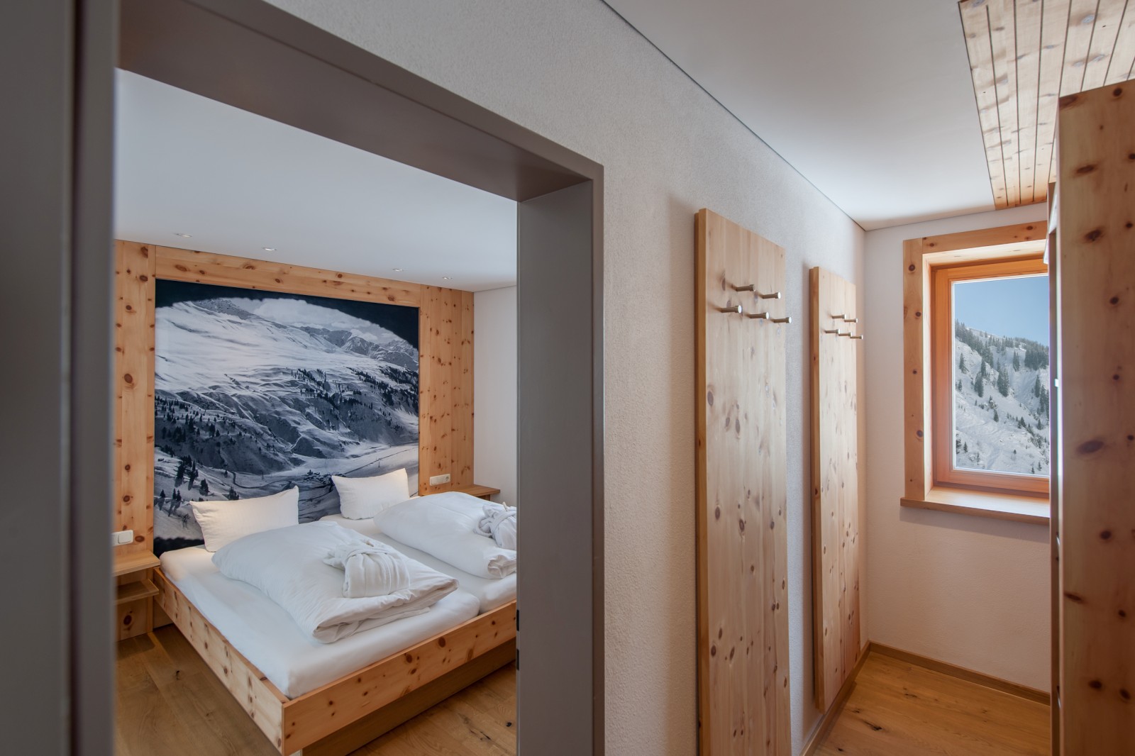 Entrance area of Family Mondschein 5 at Ski-Hotel Mondschein in Stuben am Arlberg, Austria – featuring pine wood wall panels, coat hooks, window with panoramic view, and direct access to the double bedroom
