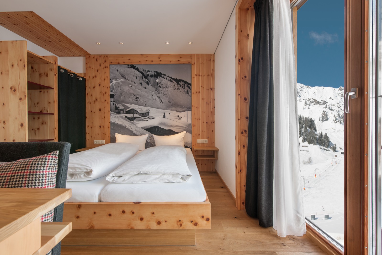 Second bedroom of the Family Mondschein Suite at Ski-Hotel Mondschein in Stuben am Arlberg, Austria – alpine-style double bed, pine wood paneling, scenic photography headboard, panoramic mountain view through glass balcony door