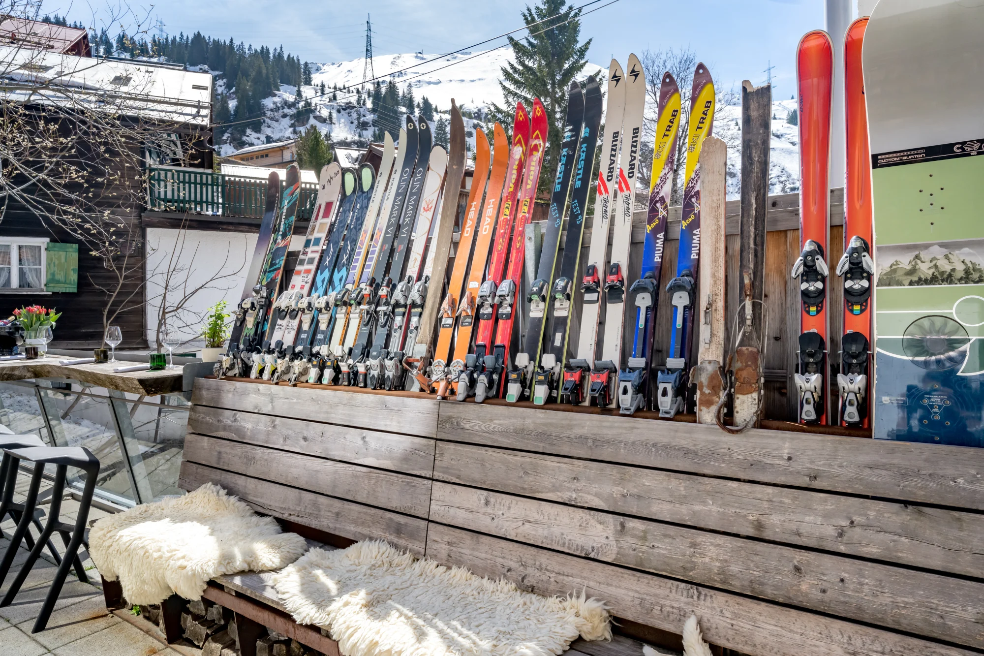 Colorful skis lined up on a sunny mountain terrace with sheepskin-covered benches at Ski-Hotel Mondschein in Stuben am Arlberg, Austria