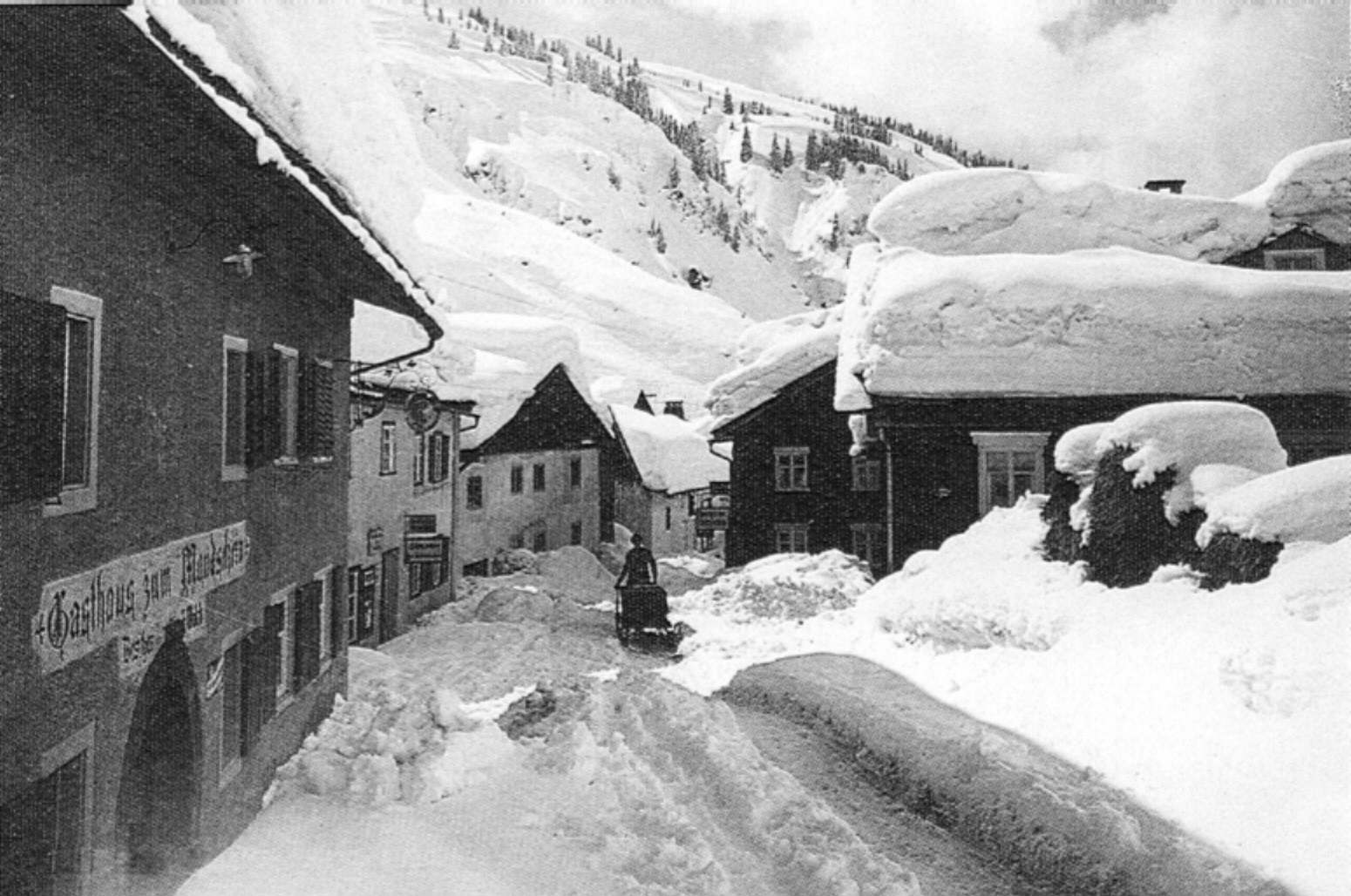 Black-and-white winter photograph showing the snow-covered village road of Stuben am Arlberg and the historic Gasthof Mondschein