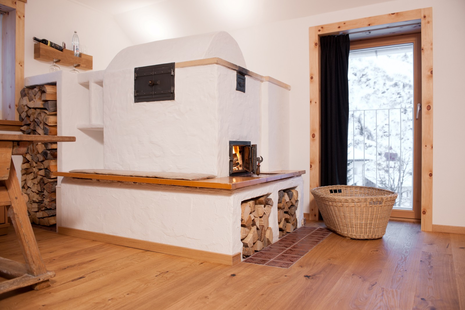 Traditional wood-burning fireplace in the Mondschein Suite at Ski-Hotel Mondschein in Stuben am Arlberg, Austria – with natural wood storage, tiled hearth, seating bench, and alpine pine wood interior