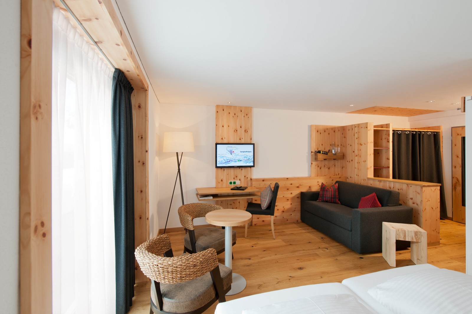 Panorama Double Room with sofa at Ski-Hotel Mondschein in Stuben am Arlberg, Austria – featuring a double bed, seating area, sofa bed, writing desk, TV, and pine wood interior design with natural light from large windows