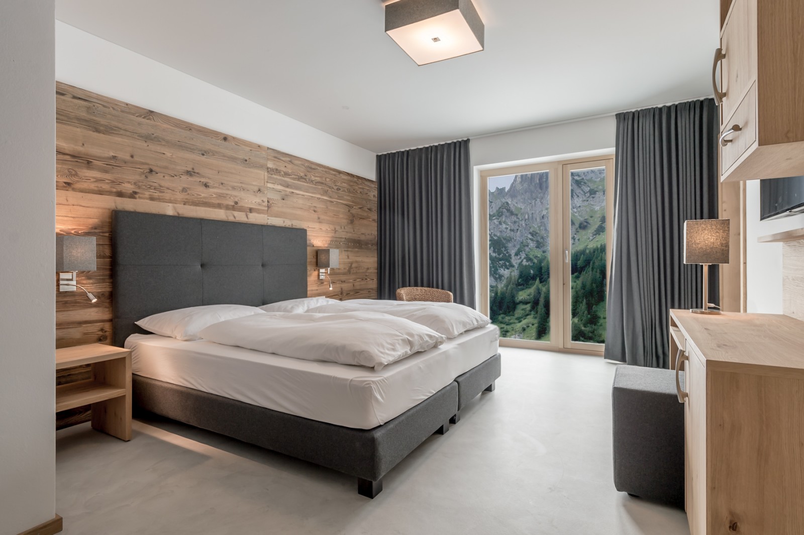 Private Double Room at Chalet Mondschein in Stuben am Arlberg, Austria – with twin bed, panoramic window, wooden wall paneling, desk, TV, and stunning view of the snowy mountains