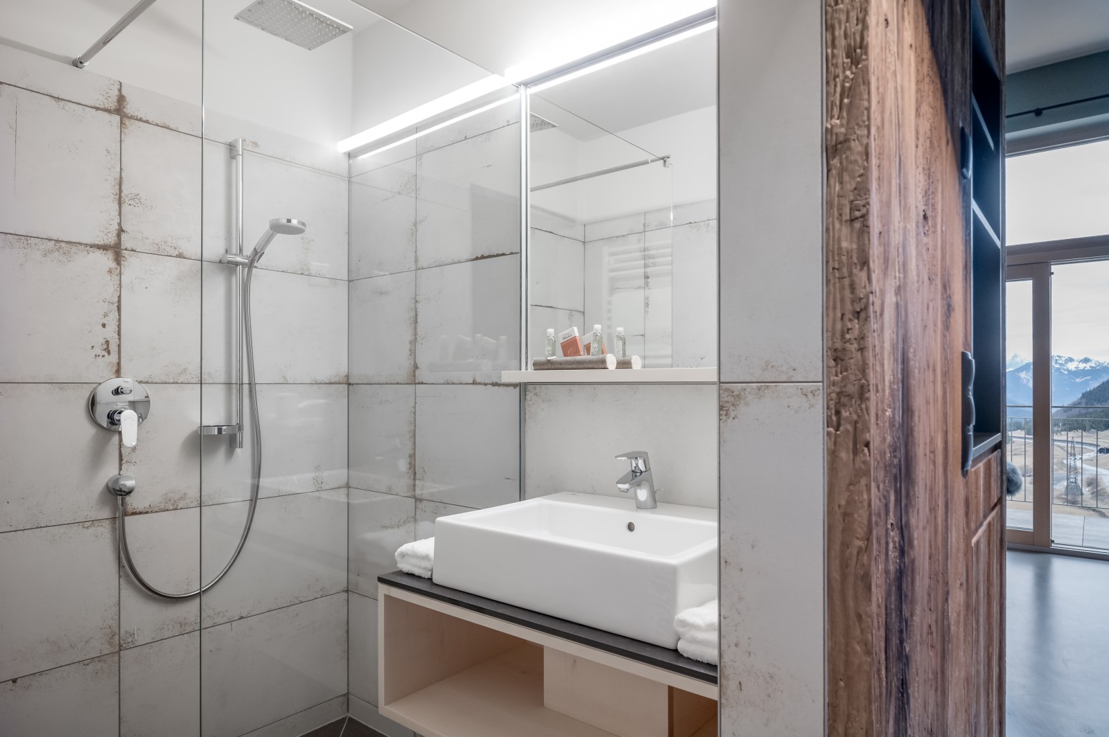Modern bathroom in the Private SPA Double Deluxe at Chalet Mondschein, Stuben am Arlberg – with walk-in rain shower, stone-look tiles, designer sink, and mountain view through floor-to-ceiling windows