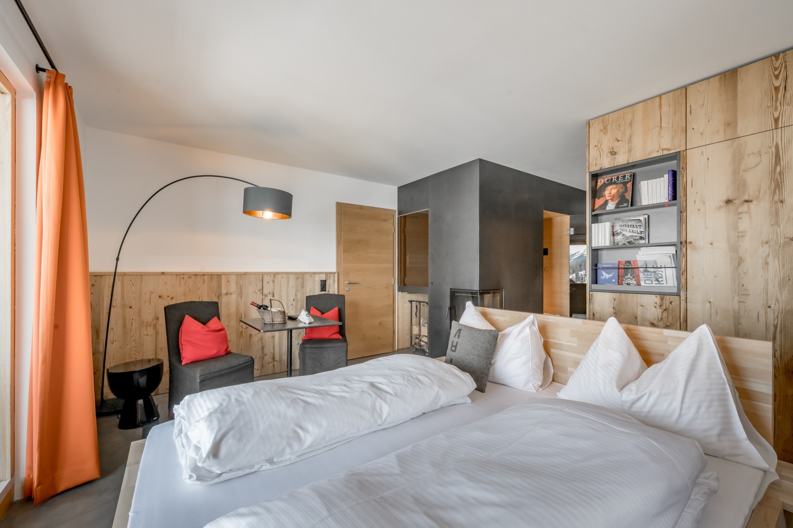 Private SPA Double Deluxe at Chalet Mondschein in Stuben am Arlberg, Austria – twin bed, small dining area with chairs upholstered in loden fabric, built-in fireplace, bookshelf, and natural oak wall paneling