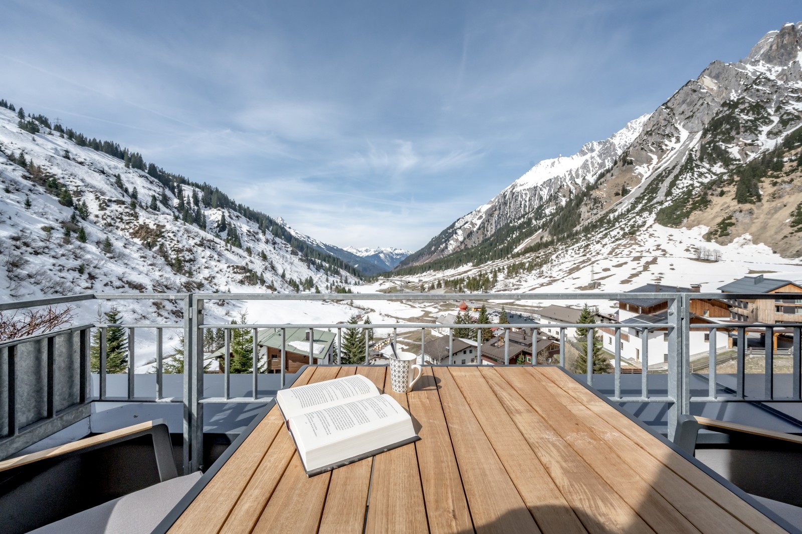Scenic mountain view from the balcony of the Private SPA Suite Exclusive at Chalet Mondschein, featuring a wooden table with a book and cup