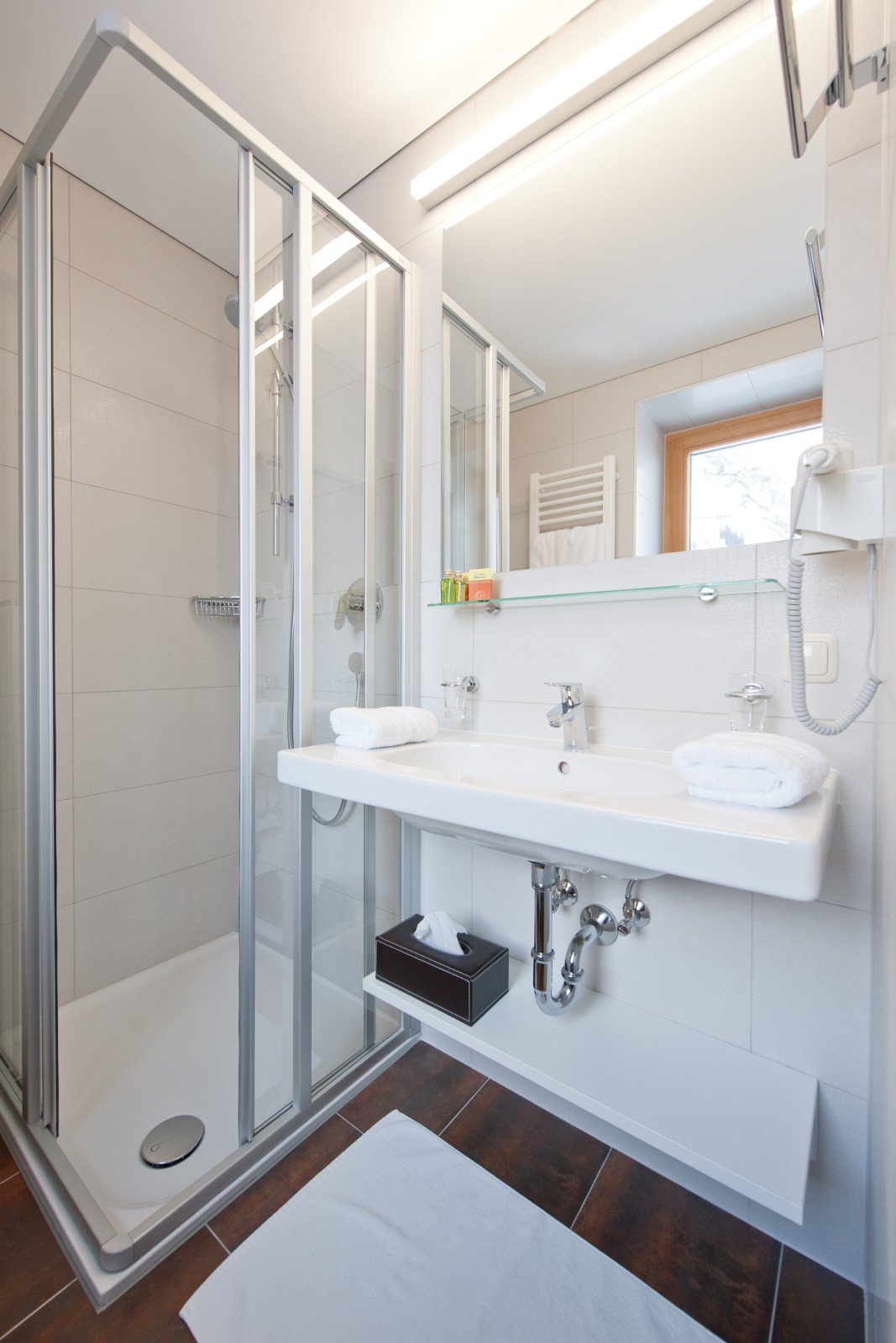 Modern bathroom of the Smart Double Room at Ski-Hotel Mondschein in Stuben am Arlberg, Austria – with glass shower, large mirror, towel heater, and bright natural light