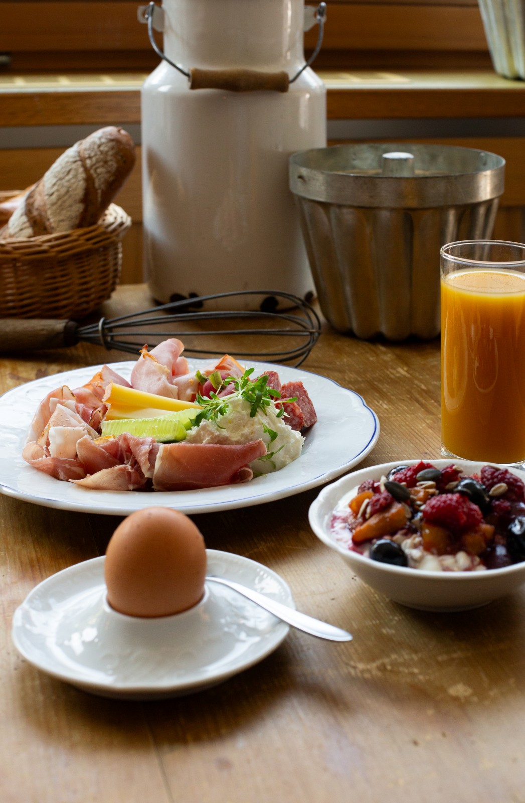 Traditional alpine breakfast with cold cuts, cheese, fresh bread, soft-boiled egg, homemade muesli with berries, and a glass of orange juice on a rustic wooden table