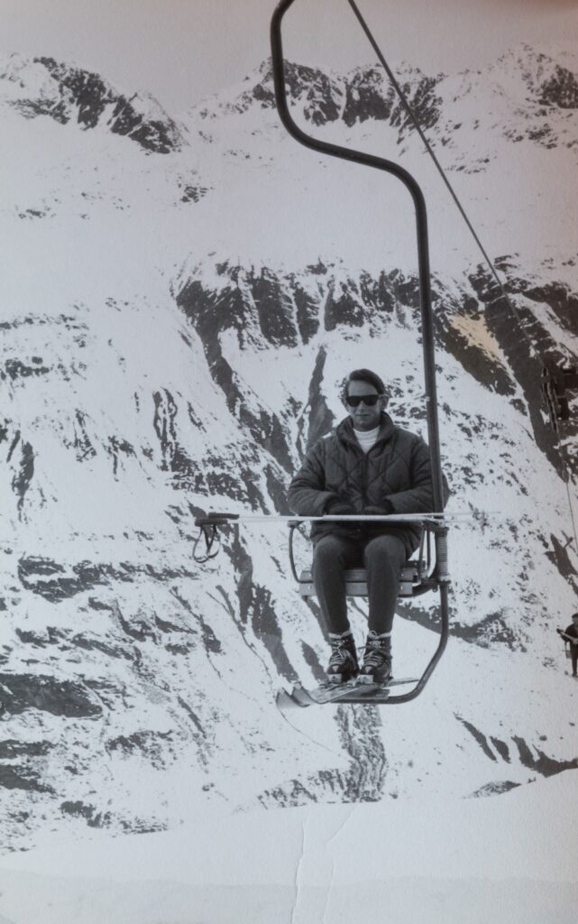 Black-and-white photo of a skier riding one of the earliest single chair lifts in the Arlberg ski area with snow-covered mountain backdrop