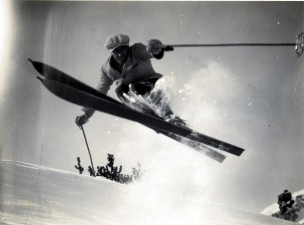 Black and white photo of Hannes Schneider mid-jump on skis, demonstrating alpine skiing technique in Japan, historic action shot