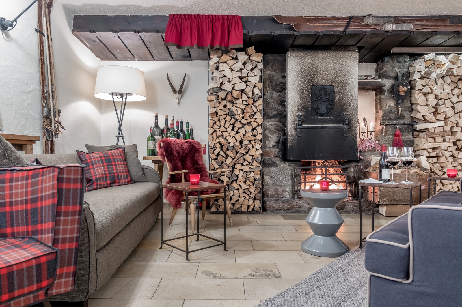 Inviting fireplace lounge with stacked firewood, vintage décor, cozy armchairs and red plaid cushions at Ski-Hotel Mondschein in Stuben am Arlberg