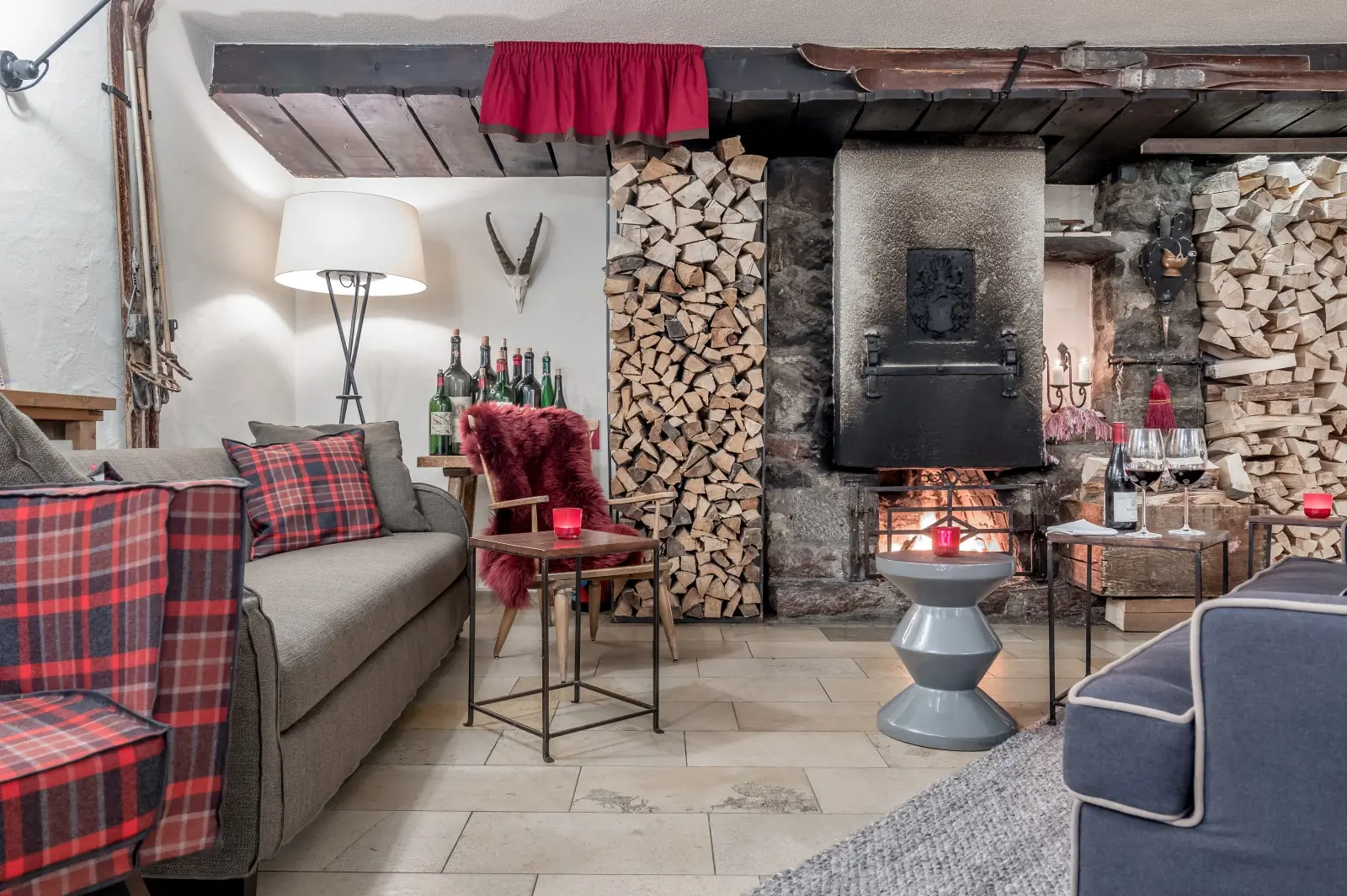 Inviting fireplace lounge with stacked firewood, vintage décor, cozy armchairs and red plaid cushions at Ski-Hotel Mondschein in Stuben am Arlberg