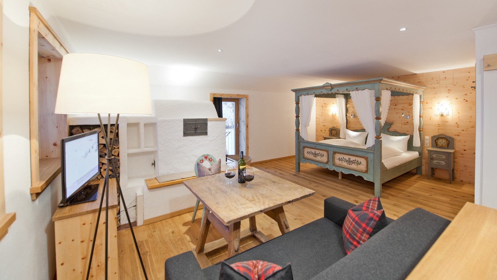 Mondschein Suite at Ski-Hotel Mondschein in Stuben am Arlberg, Austria – with a romantic hand-painted four-poster bed, traditional tiled fireplace, rustic wooden table, pine wood interior, and cozy mountain atmosphere