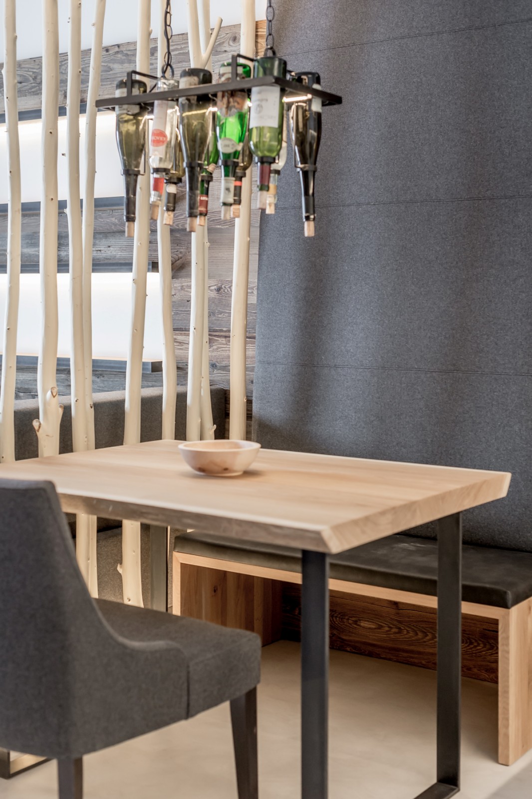 Stylish dining area in the Private SPA Suite Premium at Chalet Mondschein, Stuben am Arlberg – with natural wood table, designer felt-covered chairs and bench, and a wine bottle chandelier under modern alpine design