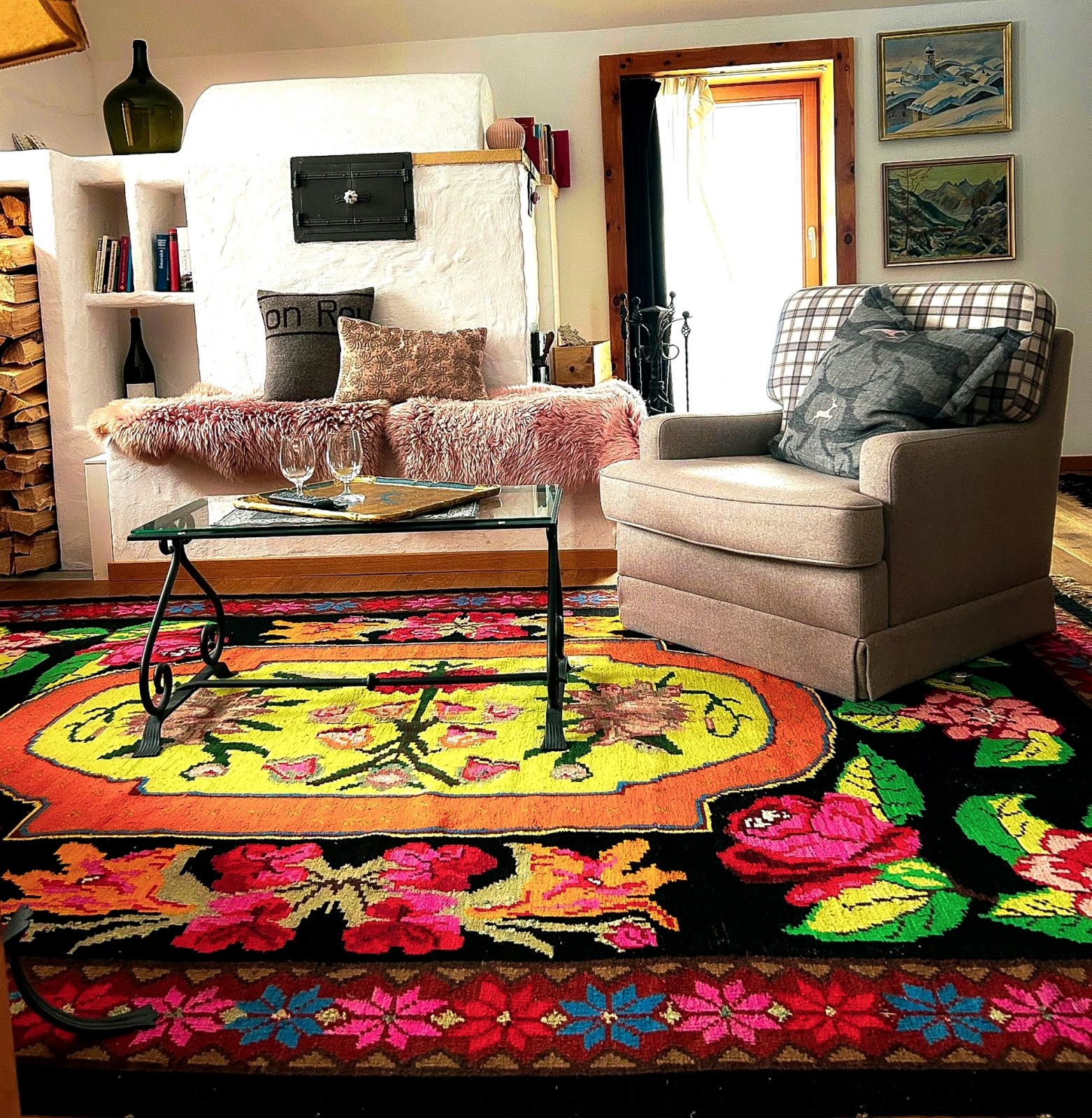 Lounge area of the Mondschein Suite at Ski-Hotel Mondschein in Stuben am Arlberg, Austria – with vintage tiled fireplace, armchair, colorful handwoven carpet, bookshelf, glass table, fur throws, and pine wood details