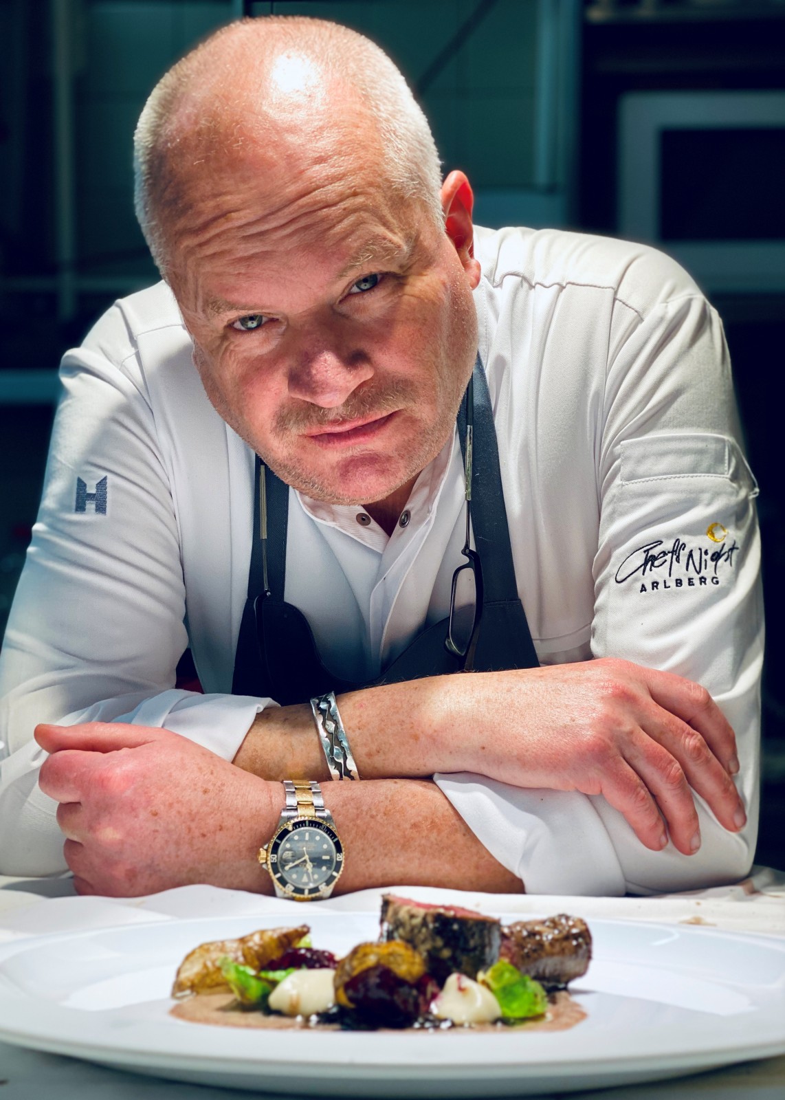 Portrait of Michelin-starred chef Dieter Koschina at the Chef’s Night Arlberg event at Ski-Hotel Mondschein in Stuben, Austria – presenting a gourmet dish in an alpine fine-dining kitchen setting