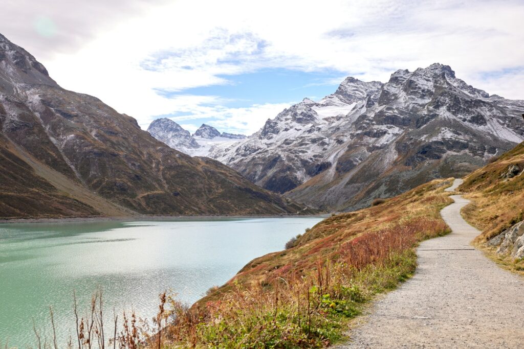 Winding hiking trail along the turquoise Silvretta reservoir in Vorarlberg, Austria, surrounded by snow-dusted alpine peaks and clear skies – a peaceful mountain landscape in late summer