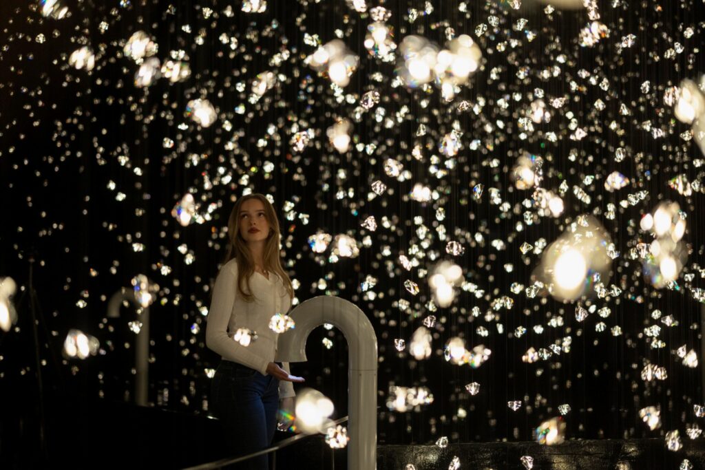 Woman standing in a dark room surrounded by suspended crystal elements and sparkling lights at Swarovski Crystal Worlds in Wattens, Austria