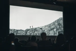 Audience watching a mountain film at the St. Anton Film Festival in Austria – black-and-white scene of two hikers on rugged alpine peaks