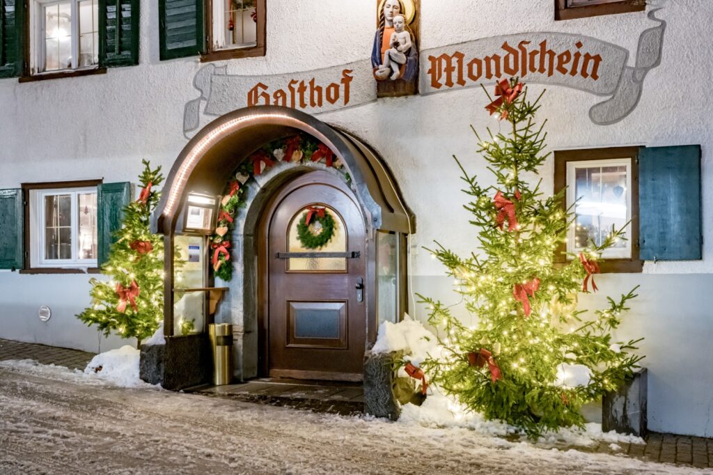 Festively decorated wooden doorway with wreaths, Christmas trees, and twinkling lights at the Gasthof Mondschein entrance in Stuben am Arlberg