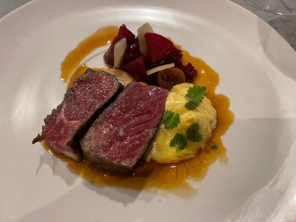 Medium-rare beef with creamy polenta and beetroot garnish on a white plate – fine dining at Ski-Hotel Mondschein